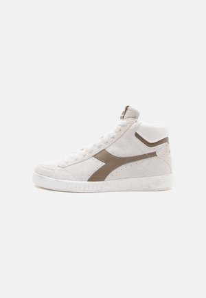High-top sneaker in light beige suede with dark brown accents, featuring a textured rubber sole and lace-up front.