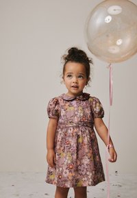 Vestido floral rosa con mangas abullonadas, cuello y falda fruncida. Sostenido con un globo con cinta. Tela suave con patrones coloridos.