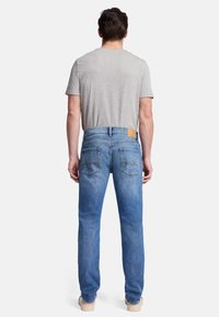 Jeans in denim azzurro chiaro con taglio dritto, dotati di due tasche posteriori e una toppa in pelle beige in vita. Maglietta grigia parzialmente visibile.
