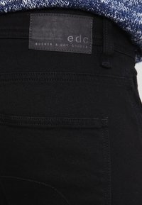 Pantalones vaqueros negros con un parche de aspecto cuero con la marca "edc". Tejido texturizado con un acabado suave y detalles mínimos de costura.