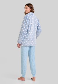 Camiseta de pijama de felpa azul claro con lunares blancos, combinada con pantalones azul claros que presentan un pequeño patrón de lunares y puños elásticos.