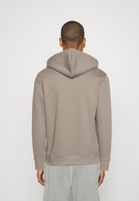 Barna kapucnis pulóver puha anyagból, nagy kapucnival, hosszú ujjakkal és bordázott mandzsettákkal és szegéllyel. Egyszerű dizájn minta nélkül.