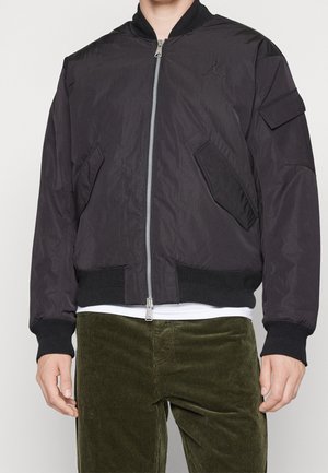 Giacca bomber nera con zip frontale, polsini e fondo a coste, tasche laterali e una tasca sulla spalla. Presenta un logo sul petto.
