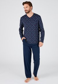 Maglia da pigiama a maniche lunghe di colore blu navy con motivo di ancore bianche e rosse, abbinata a pantaloni lunghi in tinta unita blu navy, realizzati in tessuto morbido.