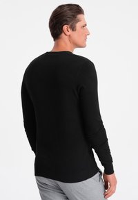 Schwarzer Langarmpullover mit geripptem Rundhalsausschnitt, taillierten Ärmeln und flachem Saum. Der Stoff scheint eine glatte, weiche Textur zu haben.
