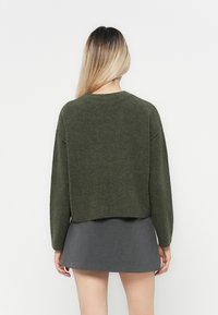 Zielony krótki sweter z okrągłym dekoltem i długimi rękawami, wykonany z miękkiego, strukturalnego materiału, w zestawie z szara spódnicą.