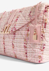 Roosa tweed õlakott, millel on tikanditunne, kuldne riistvara ja nahkveeretega rihm, millel on ruudukujuline silt ja luku detail.