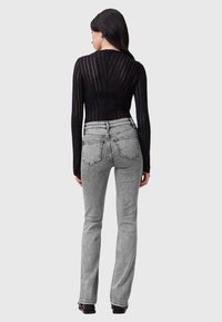 Top nero a maniche lunghe con strisce trasparenti abbinato a jeans grigi aderenti a vita alta. L'outfit presenta due tasche posteriori e una leggera ampiezza all'orlo.