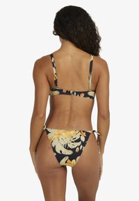 Bloem bikini met een donkere achtergrond, versierd met gele en witte bloemen, verstelbare bandjes en striksluiting aan de zijkanten. Gladde stoftextuur.