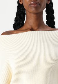 Pull en maille côtelée crème, décolleté Bardot, avec une finition texturée et un large col, présentant un design doux et décontracté.