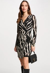 Sort og krèmefarvet omslagkjole med zebra-striber, lange ærmer og en tætsiddende silhuet, suppleret med en sort håndtaske og knæhøje støvler.