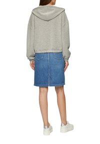 Haut à capuche gris court, associé à une jupe en denim bleu et des baskets blanches avec des accents argentés. Tenue décontractée au design simple.