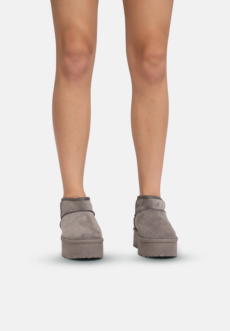 Botas de tobillo de ante gris con suela de plataforma y un suave dobladillo. La parte superior cuenta con detalles de costura y un diseño de punta redondeada.