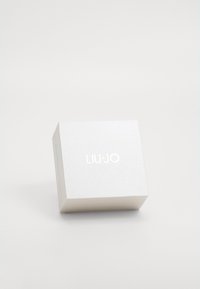 Bijela teksturirana kutija s blagim sjajem, s utisnutim imenom branda "LIU•JO" u srebrnoj boji na vrhu. Kvadratnog oblika, minimalističkog dizajna.