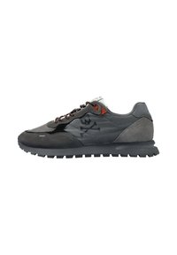 Zapatilla gris con una mezcla de materiales de malla y ante. Presenta cordones marrones, un logo de calavera y huesos cruzados en negro, y una suela texturizada.