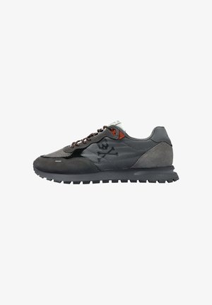 Zapatilla gris con una mezcla de materiales de malla y ante. Presenta cordones marrones, un logo de calavera y huesos cruzados en negro, y una suela texturizada.