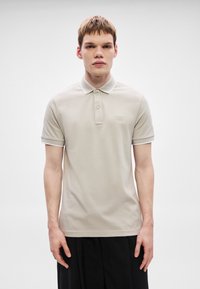 Πόλο πουκάμισο σε ανοιχτό μπεζ βαμβάκι με γιακά, πατιλέτα με δύο κουμπιά και αντίθετη λευκή λεπτομέρεια στα μανίκια. Διακριτική λεπτομέρεια λογότυπου στο στήθος.