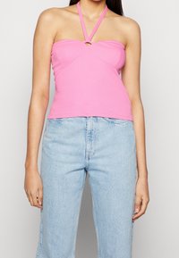 Rosa halterneck med en vriden design, med en nyckelhålsdetalj fram. Tillverkad av ett mjukt, stretchigt material, kombinerat med ljusblå jeans.