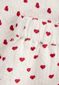Tessuto bianco con superficie testurizzata, caratterizzato da un motivo di piccoli cuori rossi. Vita elasticizzata, materiale leggero e traspirante.