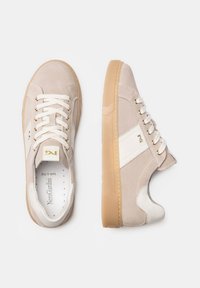 Beige suede sneakers with white accents, flat laces, and gum rubber soles. Features a rounded toe and gold logo detail on the side.