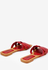 Sandales glissantes rouges avec une finition brillante, de larges lanières croisées, une semelle plate et un semelle intérieure rembourrée avec un design texturé.