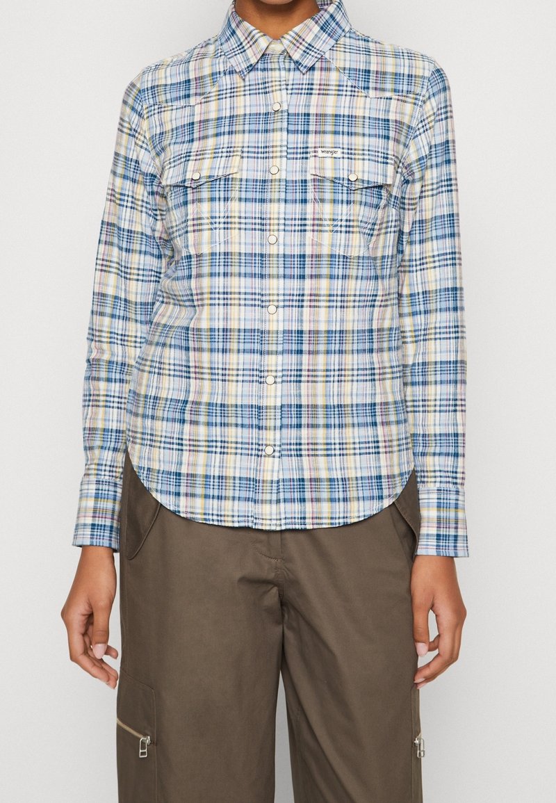 Ljusblå rutig skjorta med gula, gröna och rosa ränder, knapplist framtill, två bröstfickor och rundad nederkant.