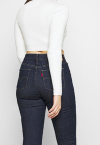 Jean en denim bleu foncé à taille haute avec des coutures visibles. Pull court à côtes blanches, ajusté à la taille, avec des manches longues.