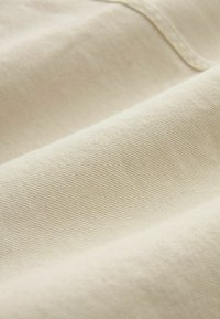 Tessuto di colore crema con una superficie morbida e texture evidente, caratterizzata da un motivo di tessitura diagonale. Il materiale appare resistente e leggermente lucido.