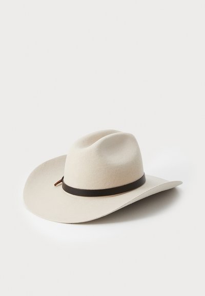 Laiaga äärega cowboy müts, mis on valmistatud pehmest beežist villast, millel on tumepruun nahast riba ja kaks dekoratiivset punkti kroonil.