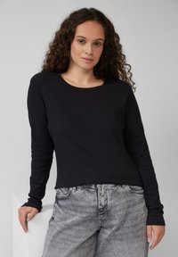 Zwarte geribbelde lange mouw top met een ronde hals, gecombineerd met lichtgrijze, iets versleten wijde jeans. Eenvoudig ontwerp, aansluitende snit.