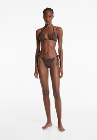 Bikini souprava s trojúhelníkovými košíčky a zavazovacími kalhotkami, s černobílým a oranžovým pruhovaným zebřím vzorem. Vyrobeno z lehkého materiálu.