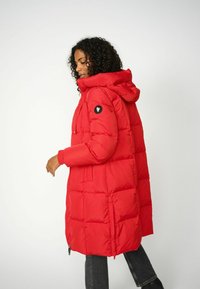 Rode pufferjas met een capuchon, voorzien van een gequilt ontwerp, elastische manchetten en een zwart logopatch op de linkermouw. Voorzien van een ritssluiting aan de voorkant.