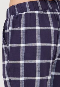 Marinblå rutiga pyjamasbyxor med ett vitt rutig mönster, tillverkade av mjukt tyg, med elastiskt midjeband och sidofickor.