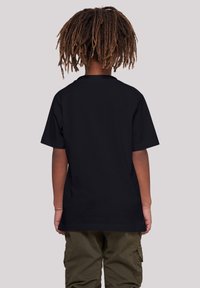Black short-sleeve t-shirt with a round neckline, loose fit, and smooth texture, worn with olive cargo pants, viewed from the back.