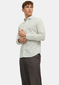 Chemise boutonnée de couleur claire avec un petit motif géométrique. Dotée de manches longues et d'un col, fabriquée en tissu lisse.