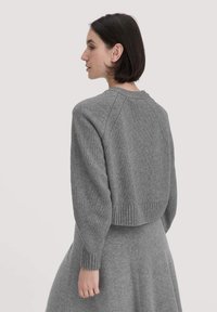 Grauer, verkürzter Pullover mit geripptem Saum und Ärmeln, der ein strukturiertes Strickmuster, Raglanärmel und einen Rundhalsausschnitt aufweist.