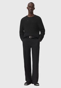 Jersey negro de punto con un sutil deterioro, combinado con pantalones negros ajustados y zapatos oscuros. Diseño minimalista con líneas simples.