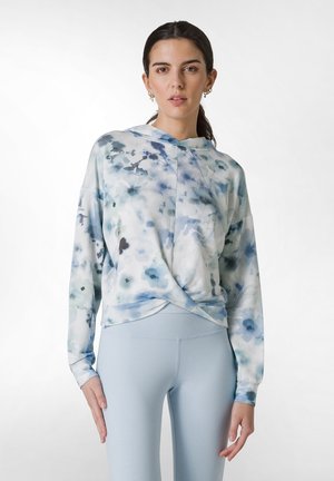 Langærmet, lyseblå blomsterbluse med en snoet frontdesign, blødt stof og hætte. Stylet med lyseblå leggings.