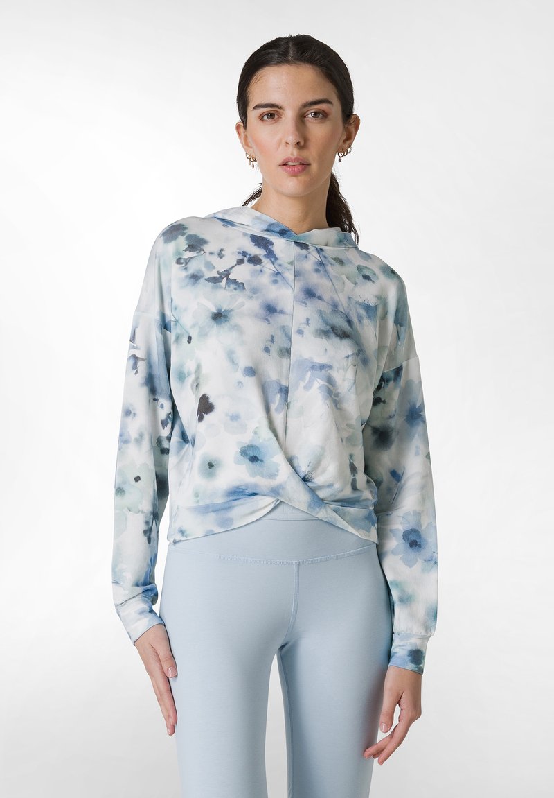 Långärmad, ljusblå blommig topp med en vriden frontdesign, mjukt tyg och en huva. Matchas med ljusblå leggings.