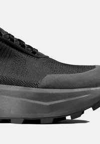 Närbild av en svart sportskor med textilöverdela, tjock dämpad sula och grov yttersula för bättre grepp.