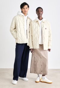 Chaquetas de crema acolchadas con botones a presión, combinadas con sudaderas. Pantalones sueltos azul marino y una falda beige. Zapatillas blancas con detalles amarillos.