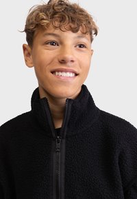 Black fleece jacket with a high collar and zippered front. Textured fabric, featuring sturdy zipper hardware. No other details visible.