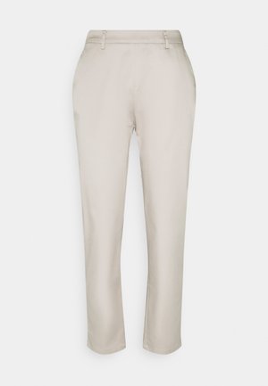 Beige slim-fit broek met riemlussen, zijzakken en een licht taps toelopende pijp, getoond op een effen lichte achtergrond.