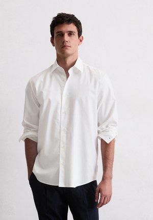 Witte button-up shirt met lange mouwen, enkele manchetten, zachte textuur en een reguliere pasvorm, tentoongesteld op een mannelijk model tegen een effen achtergrond.