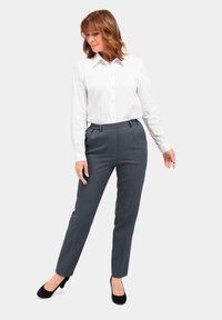 Weißes langärmliges Hemd mit Knöpfen, kombiniert mit grauen maßgeschneiderten Hosen. Die Hose verfügt über einen elastischen Bund und eine schmale Passform. Schwarze High Heels.