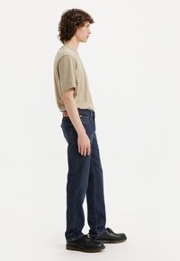 Beige cotton t-shirt with short sleeves, paired with dark blue denim jeans and black lace-up shoes, displayed in a side profile view.