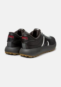 Scarpe da ginnastica nere con una tomaia sintetica testurizzata, lacci bianchi e marchio rosso sul tallone. Presentano una suola in gomma spessa con trazione.