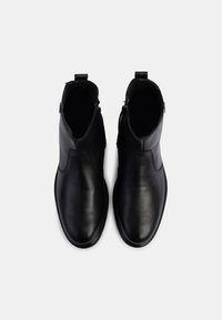 Botas de tobillo de cuero negro con un acabado suave, que cuentan con cremalleras laterales y una punta redondeada. El diseño superior incluye detalles de costura mínimos.