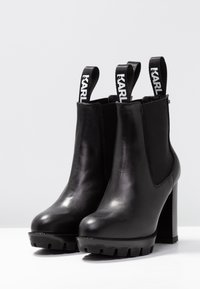 Black leather ankle boots with thick soles, high block heels, elastic side panels, and pull tabs featuring the word "KARL" in white.