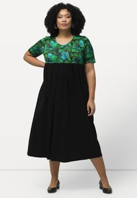 Vestido maxi con parte superior de estampado de hojas tropicales verdes y falda negra plisada. Mangas cortas, escote redondo y silueta fluida.